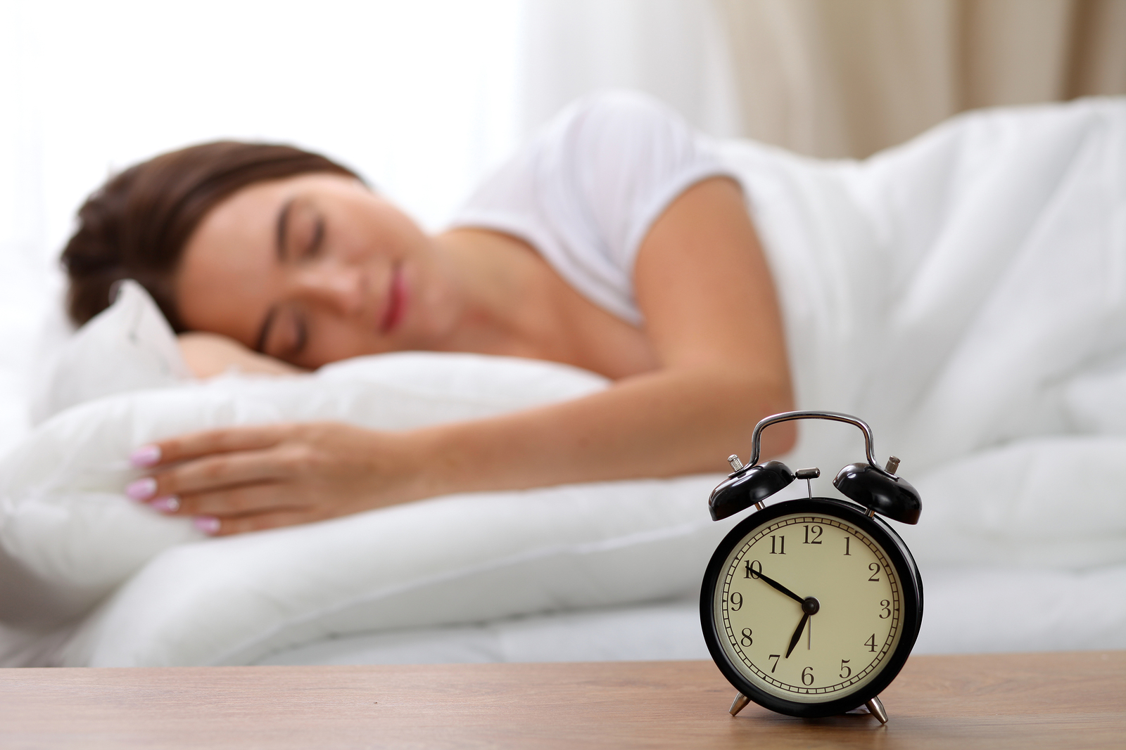 Alarm clock standing on bedside table has already rung early morning to wake up woman in bed sleeping in background Early awakening not getting enough sleep oversleep time line concept