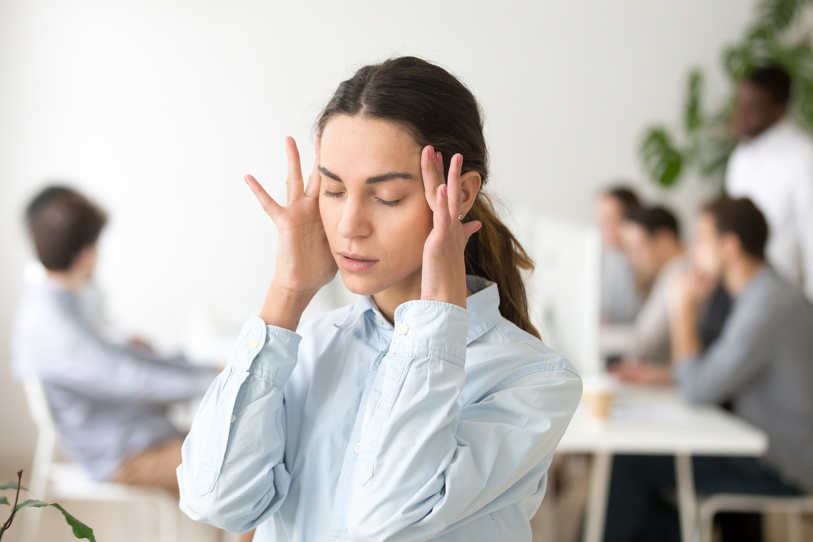 Stressed frustrated young woman employee feeling pain unwell dizzy tired of difficult office job suffering from panic attack hormone imbalance or having headache migraine massaging temples at work